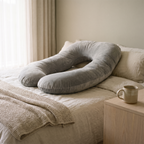 Nessa pregnancy pillow on a bed beside a folded knit throw